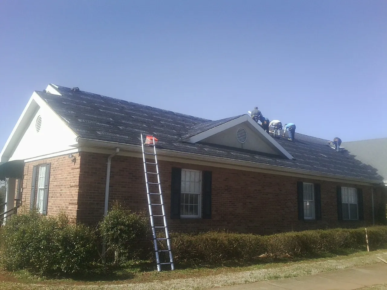 Crew tearing shingles off a brick ranch roof with a ladder set — Emergency Roof Repair work by our crew in Enon