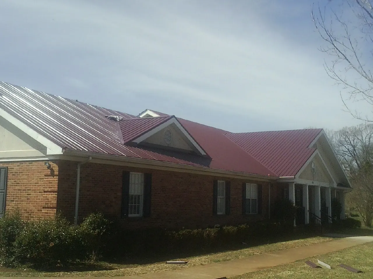 Red metal roof with gabled entries on a long brick building, from a Hail Damage Roof Repair job in Enon