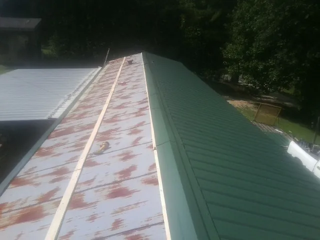 Old rusted panels beside newly installed green metal roofing — Wind Damage Roof Repair by Roofing Brothers in Enon