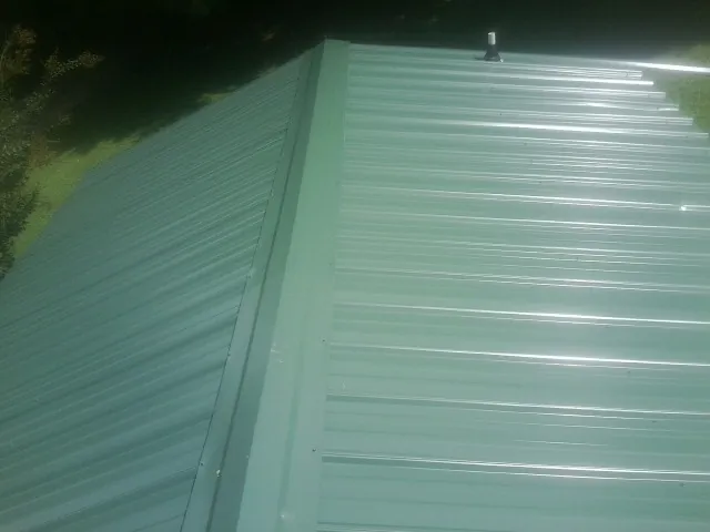 New green metal panels meeting at the ridge of a roof — Flat Roof Repair work by our crew in Enon