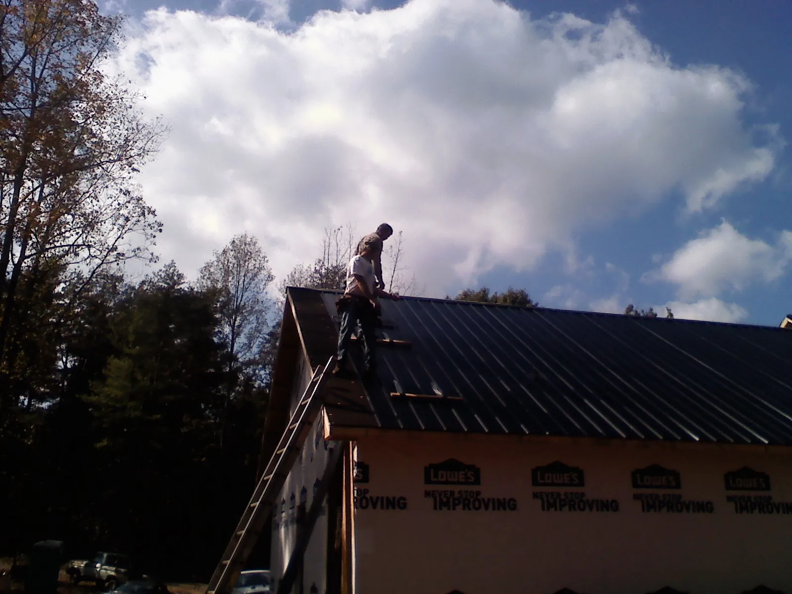 Roofer fastening dark metal panels high against a cloudy sky, from a Roof Inspection job in Enon