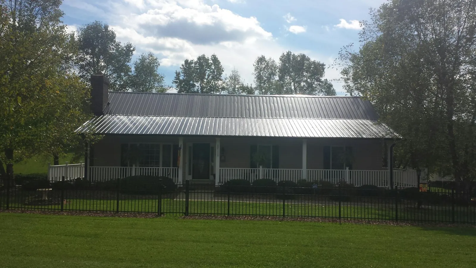 Gray metal roof on a brick ranch with a full width front porch — Gutter Guard Installation work by our crew in Enon
