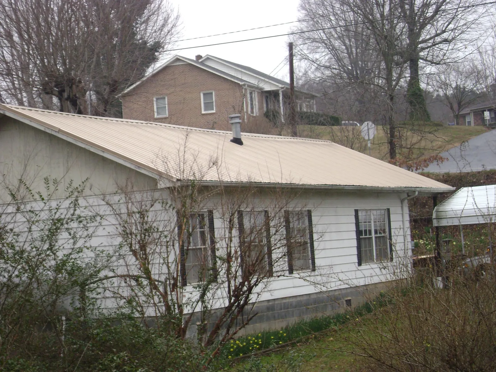 Tan metal roof on a white sided house set into a hillside — Commercial Roofing by Roofing Brothers in Enon